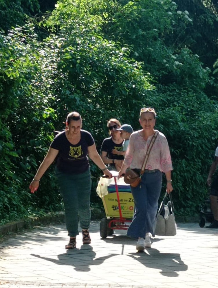 Zwei Frauen aus der Dravet-Communty ziehen den vollen Bollerwagen zum Grillplatz im Park.